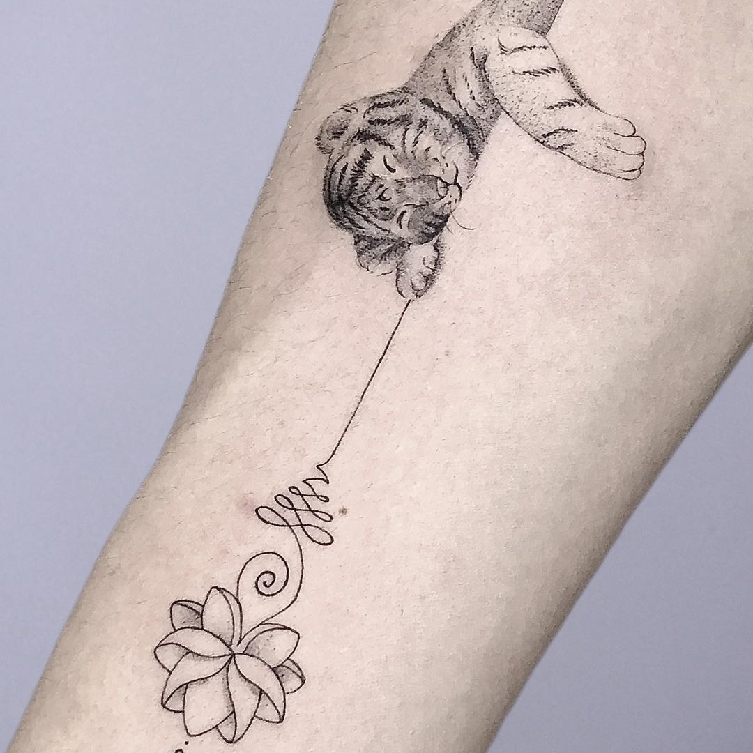 Tattoo of a tiger cub and a lotus flower on an arm