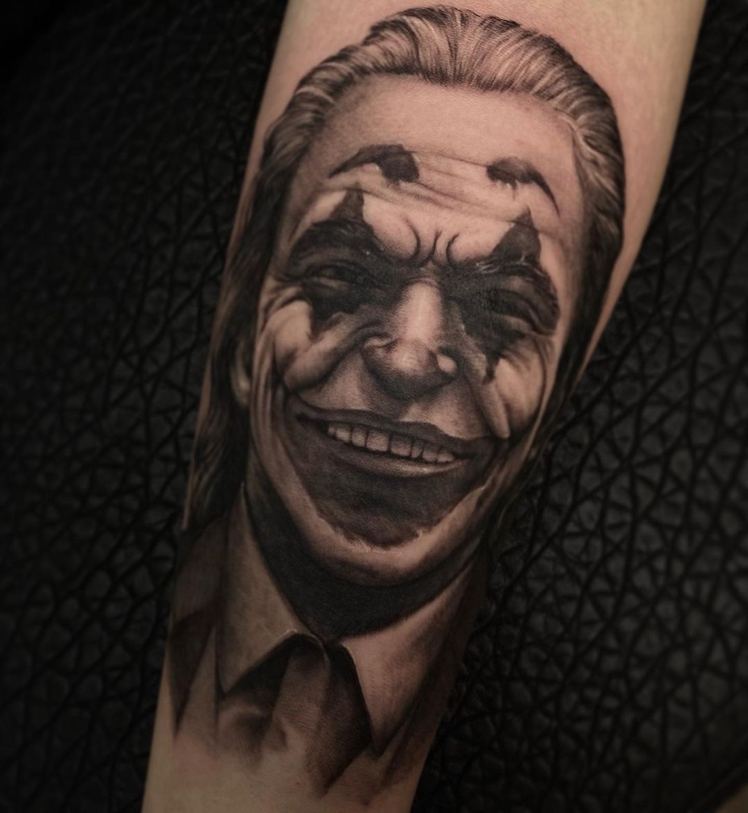 Black and grey tattoo of a smiling joker character on skin.