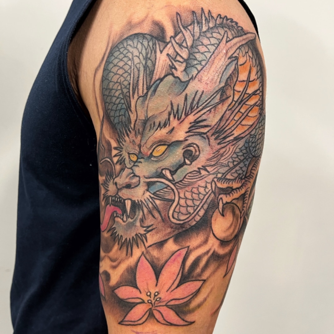 A detailed tattoo of a dragon and a flower on a person's arm.