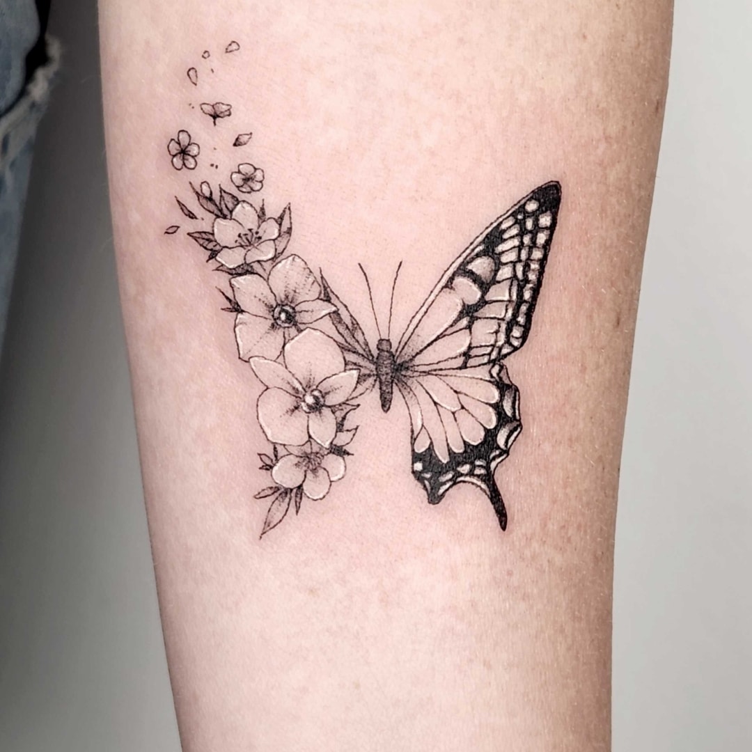 A delicate butterfly tattoo with floral elements on a leg.