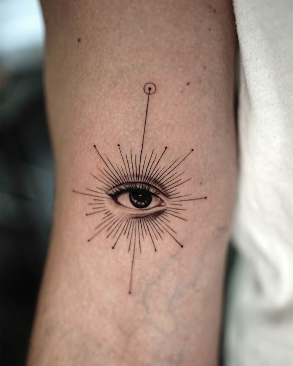 Detailed black ink tattoo of an eye with rays on arm