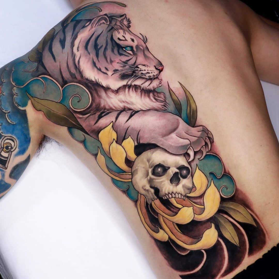 Tattoo of a tiger above a skull and flowers.